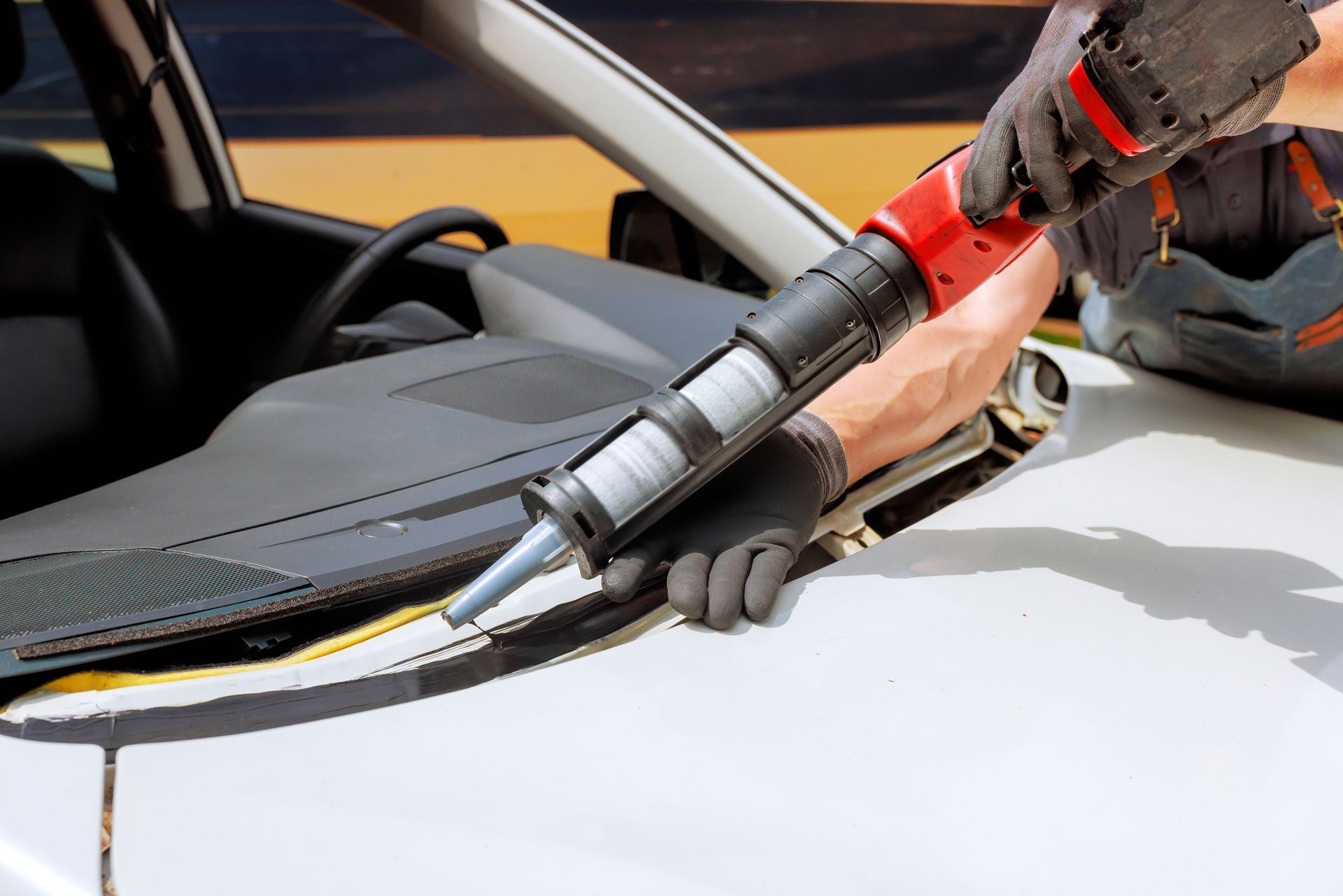 Worker using a caulking gun to seal a white car windshield edge