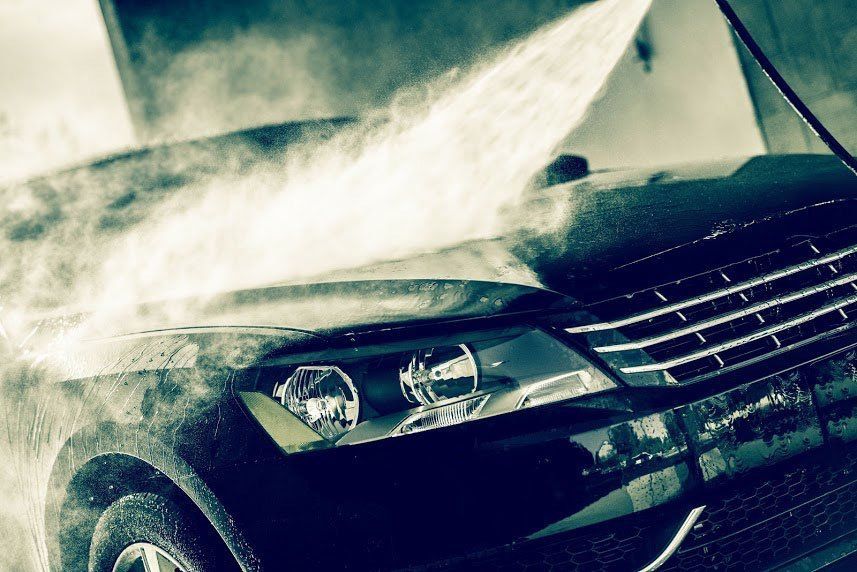 Black car with front headlights, splashed with water in a car wash or rain spray