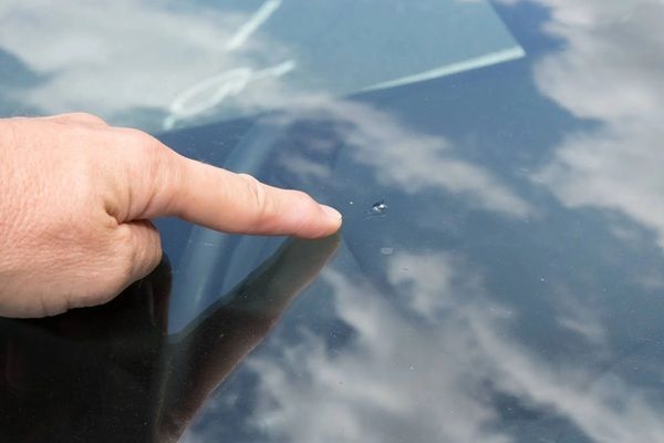 Finger pointing at a blue reflective car surface with sky reflections