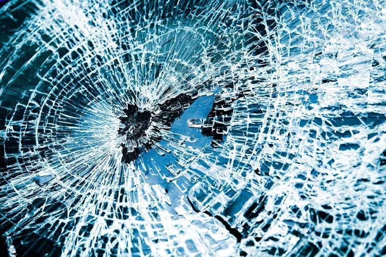 Shattered blue windshield glass with a dark impact point at the center