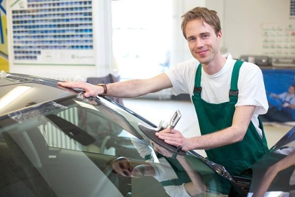 Mechanic in green overalls polishing a car windshield in a bright auto shop