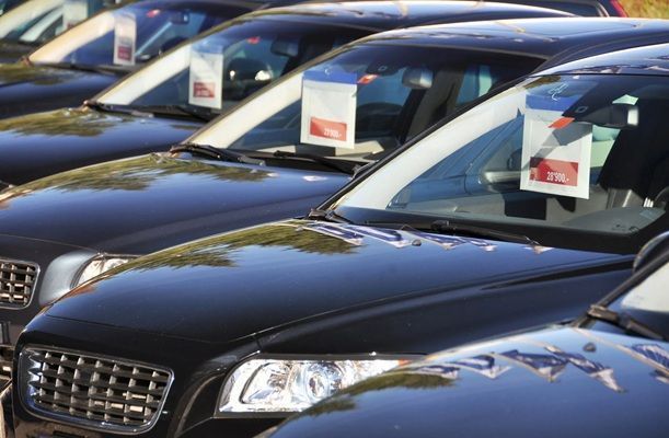 Rows of black sedans parked close together on a lot, each with a sale sign in the windshield
