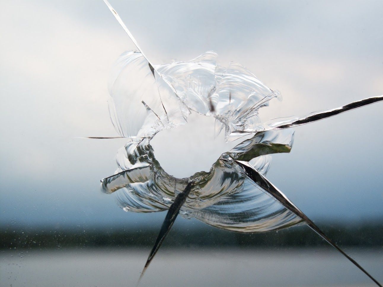 Shattered windshield with spiderweb cracks and a large impact hole over a blurred landscape
