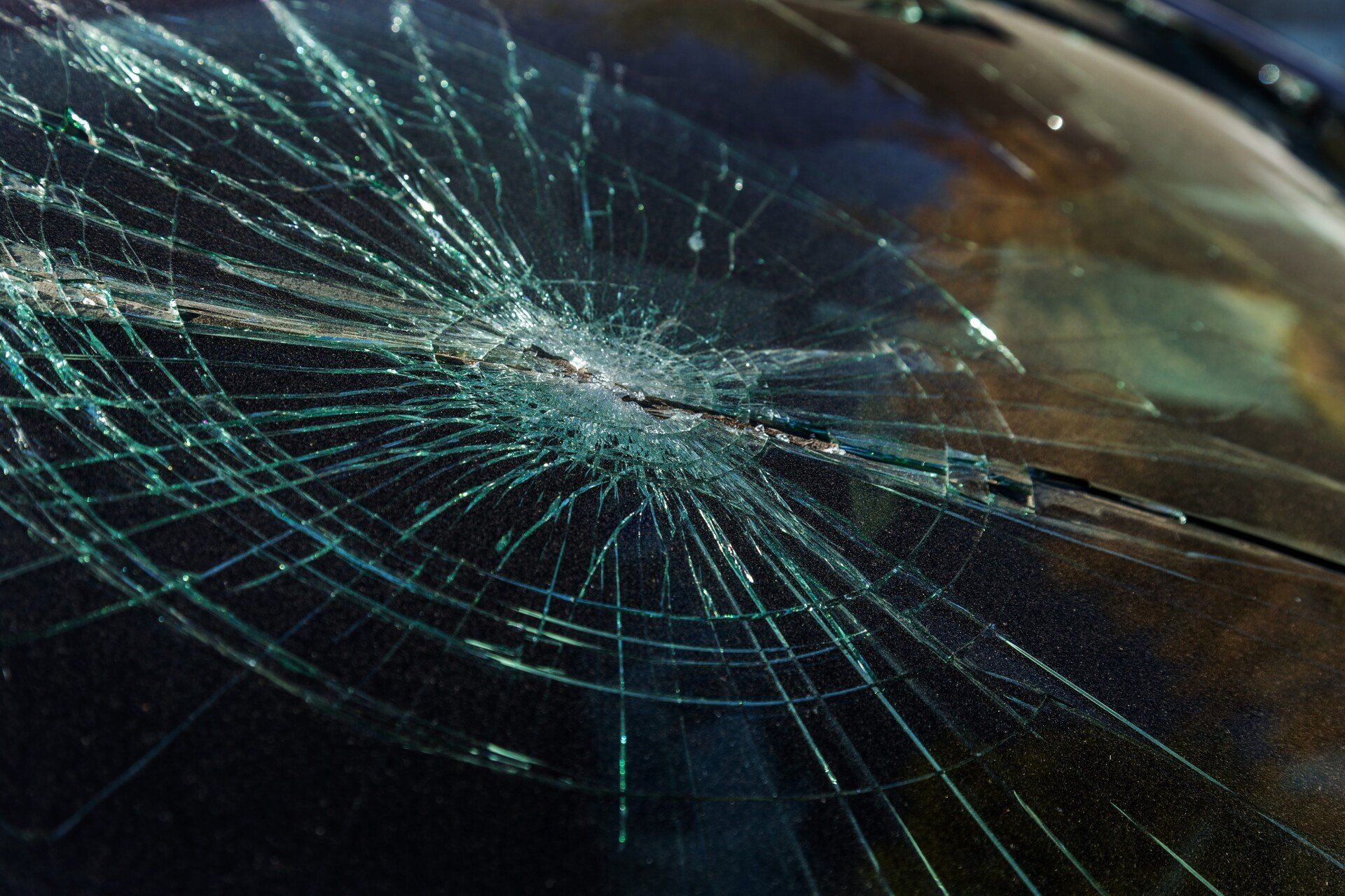Cracked car windshield with spiderweb fractures and shattered glass
