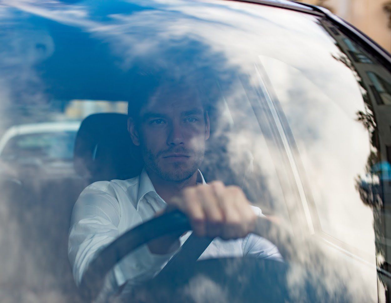 Man driving a car, seen through the windshield with reflections on the glass.