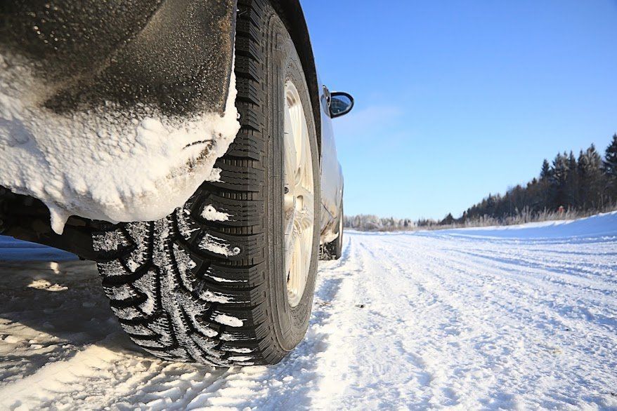 Snow-covered tire on a vehicle driving on a snowy road under a clear blue sky