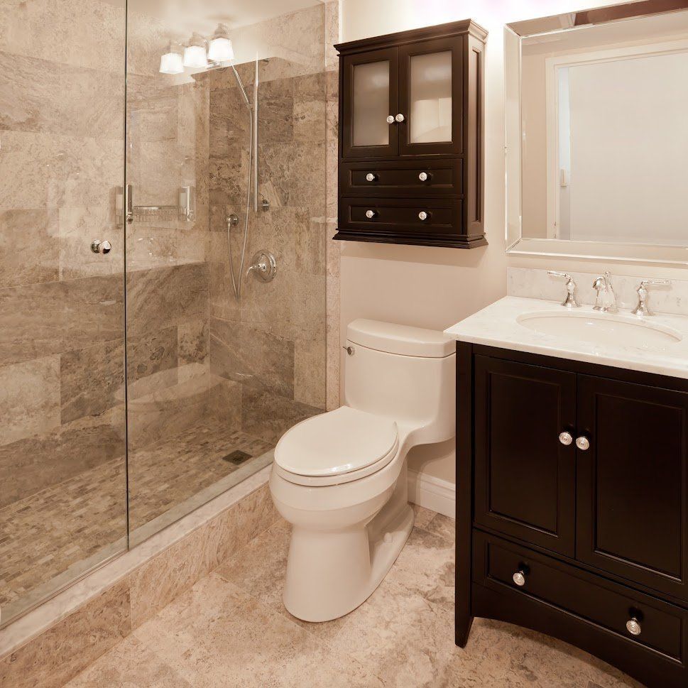 Luxury beige bathroom with glass shower, toilet, dark wood cabinets, and white vanity sink
