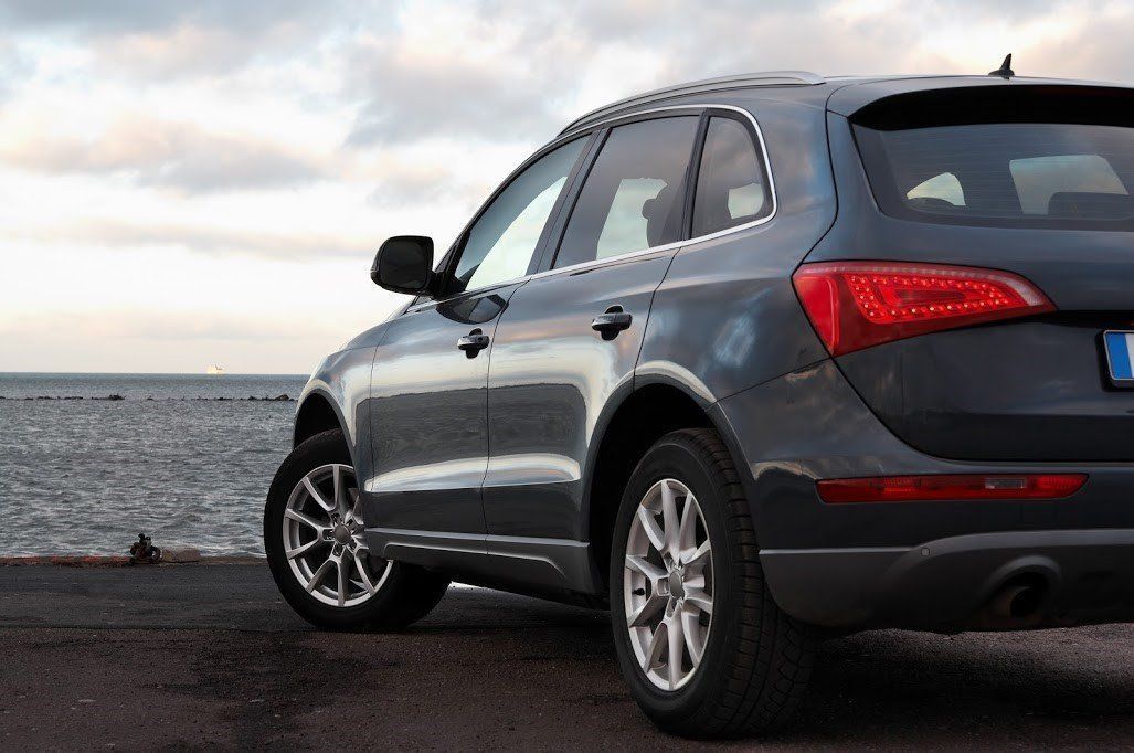 Gray SUV parked by the water at sunset, viewed from the rear side.