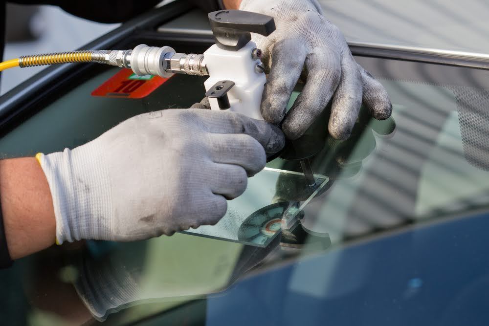 Gloved hands repair a cracked car windshield with a resin injector tool.