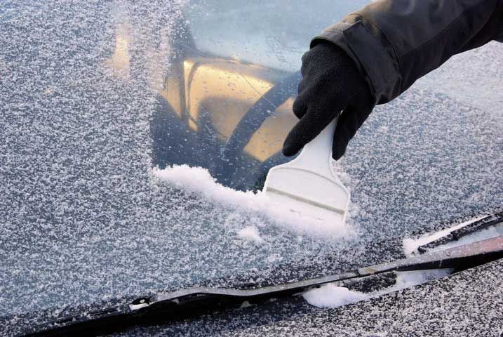 Hand scraping frost from a car windshield with a brush in winter.
