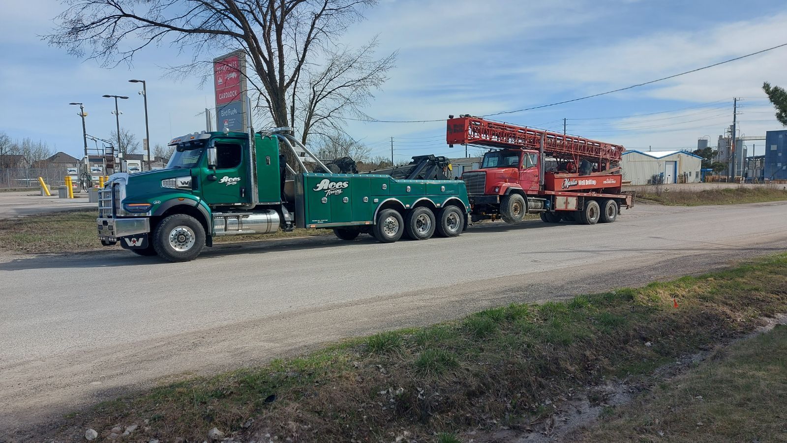 A green tow truck is driving down a road next to a red truck.