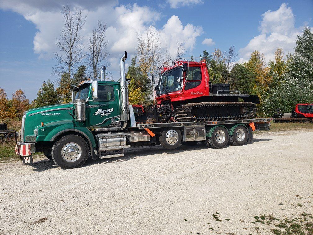 A green semi truck is carrying a red snow plow on a flatbed trailer.