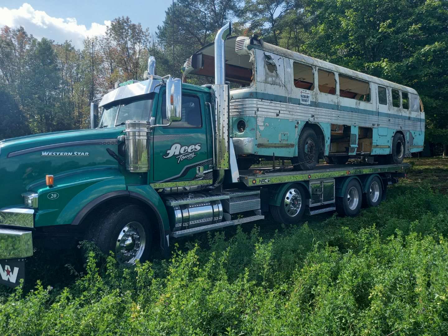 A semi truck is carrying a yellow excavator down a dirt road.