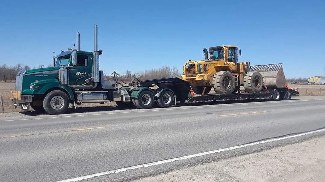 A semi truck is carrying a bulldozer down a highway.