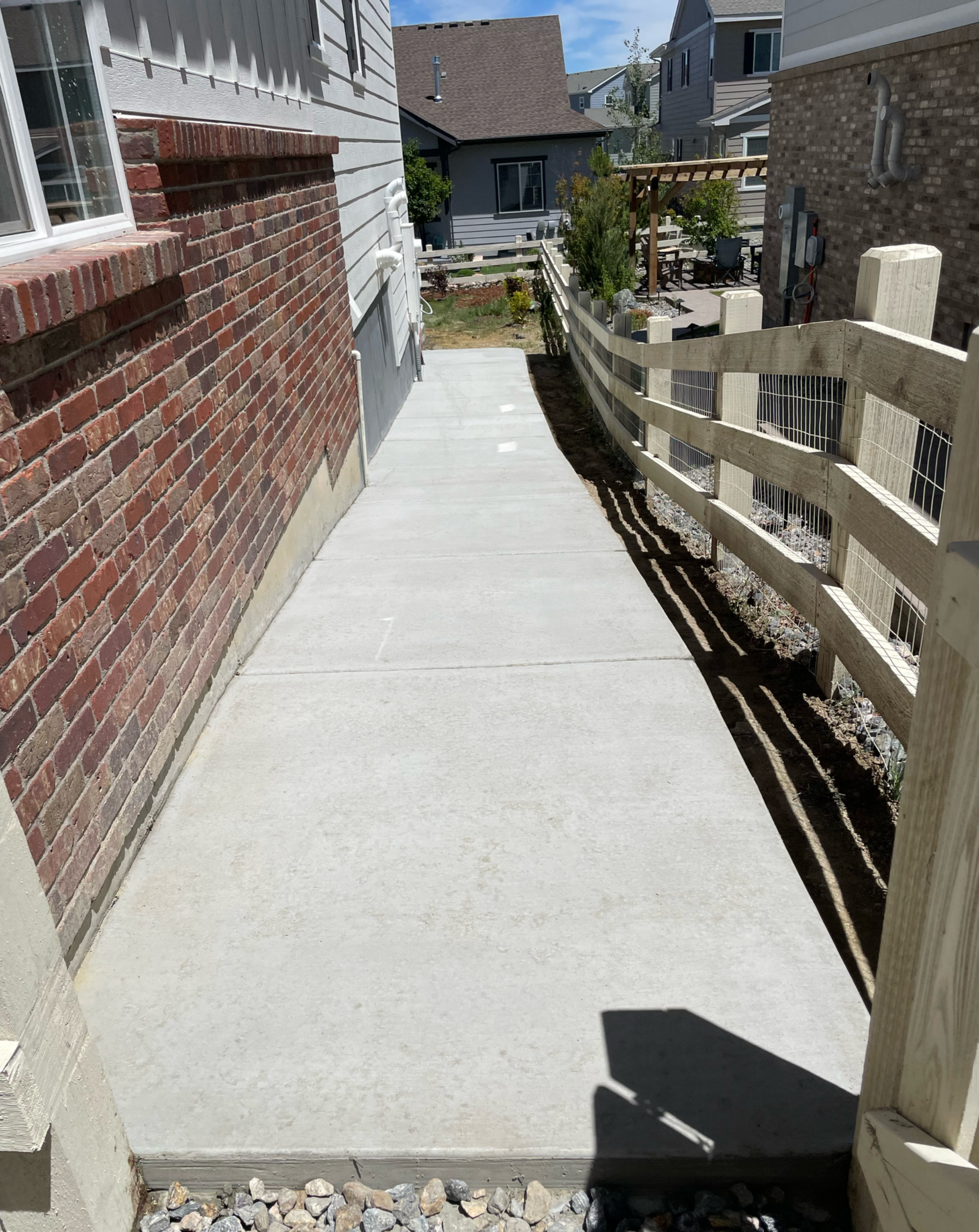 Narrow concrete side walkway running between a brick house and a fence