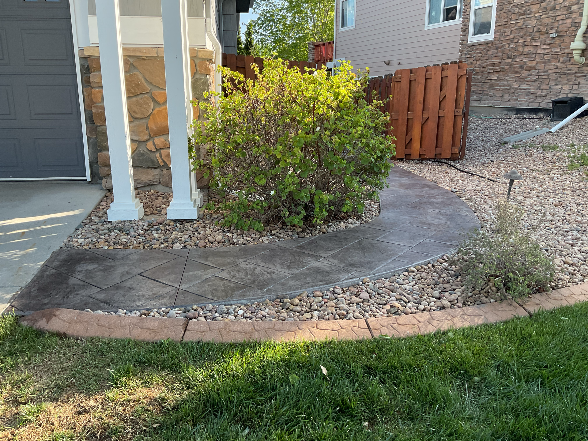Stamped concrete walkway with a brick-pattern border curving around a front porch