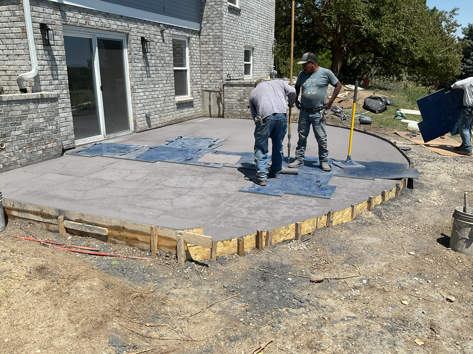 Two workers finishing a curved stamped concrete patio still held in its wood forms