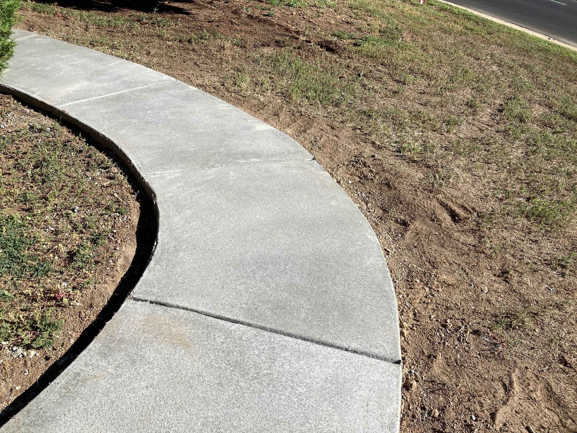 A concrete walkway leading to a house with a lush green lawn.