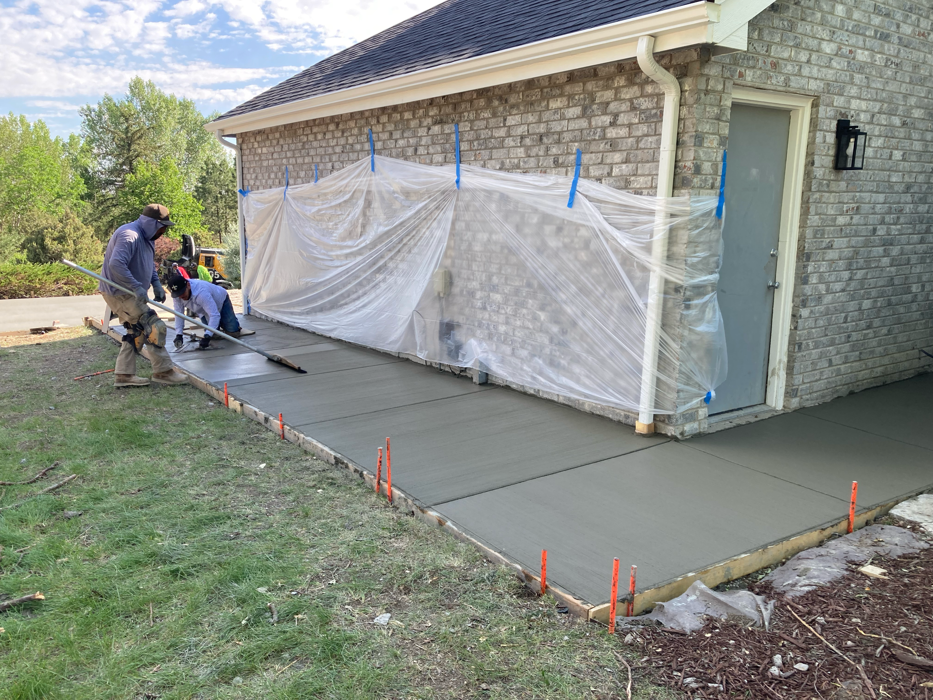 Crew finishing a long concrete walkway along the side of a brick house