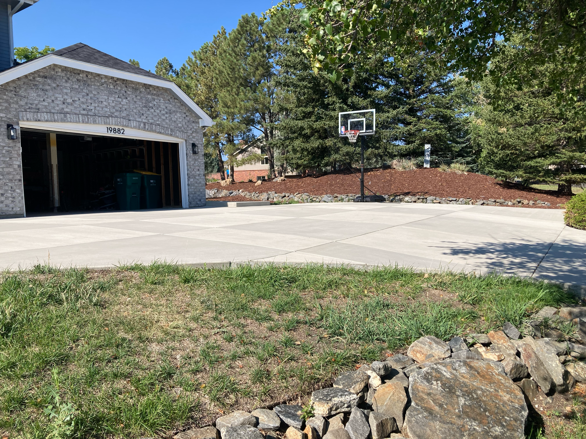 Broad finished concrete driveway in front of a three-car garage with a basketball hoop
