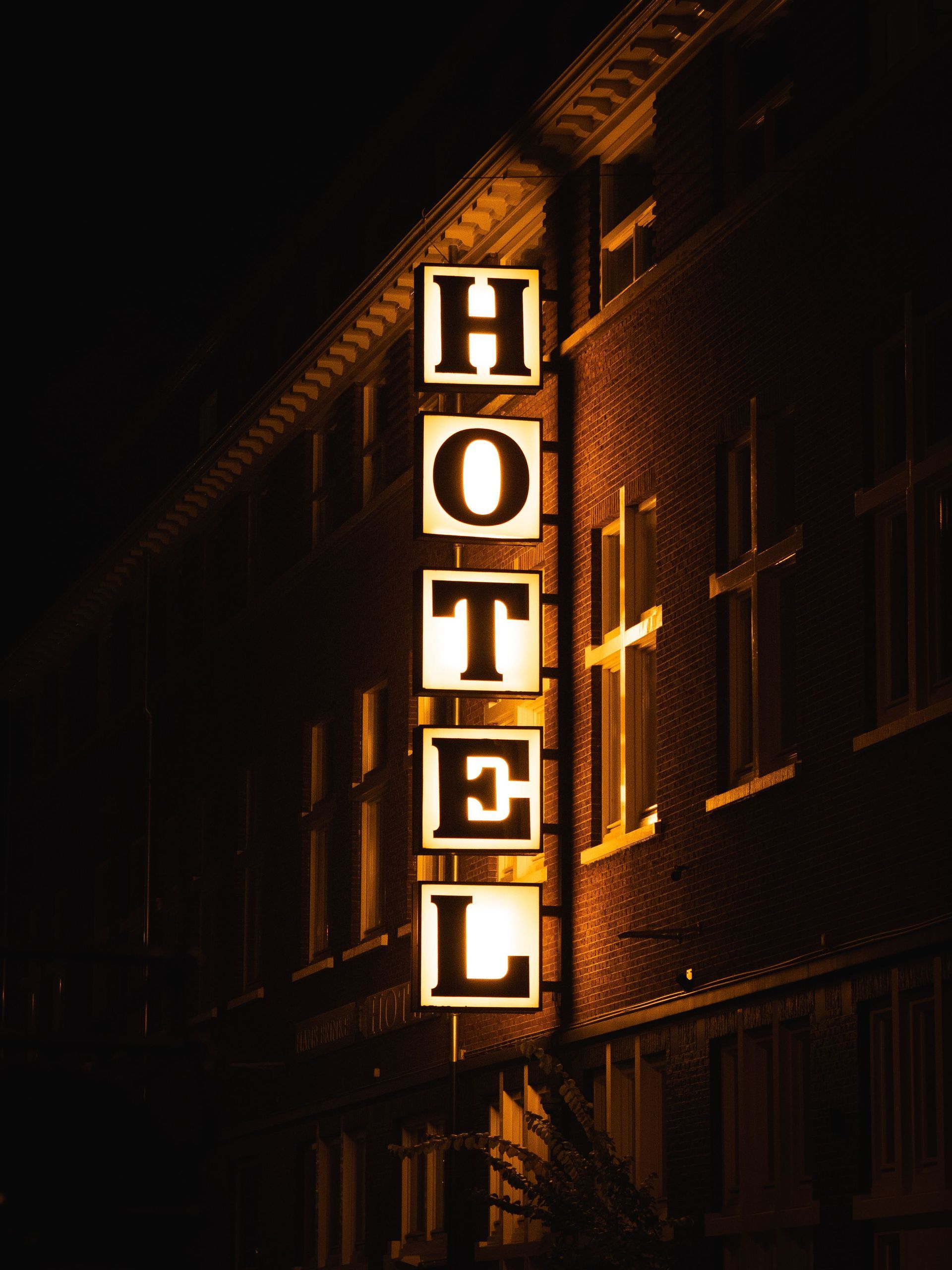 A HOTEL sign lit up at night, glowing against the brick facade of the front of the hotel.