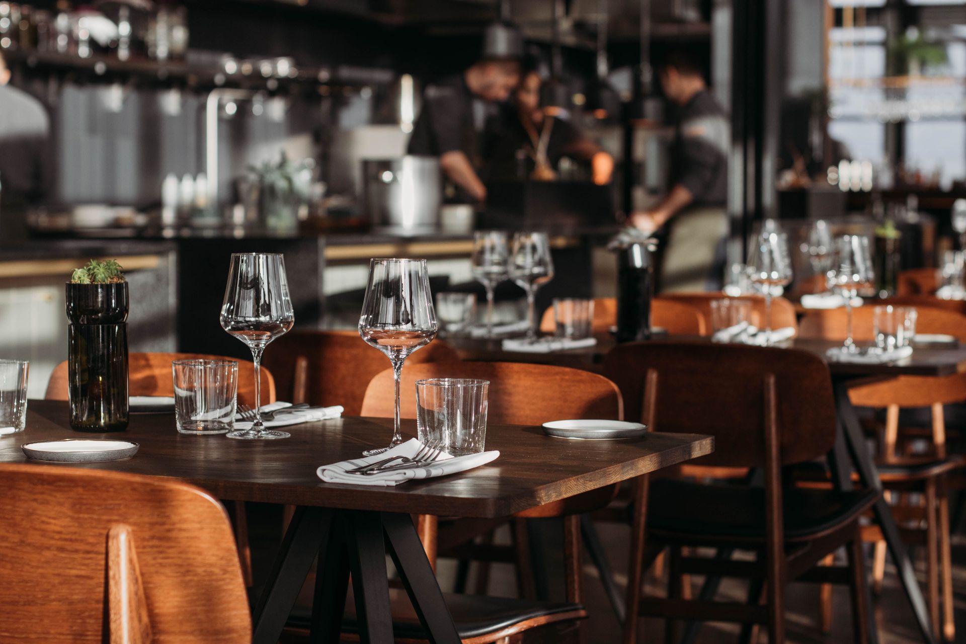 Inside view of a restaurant with prepared dinner tables and a chef interacting with customers visible in the distance.