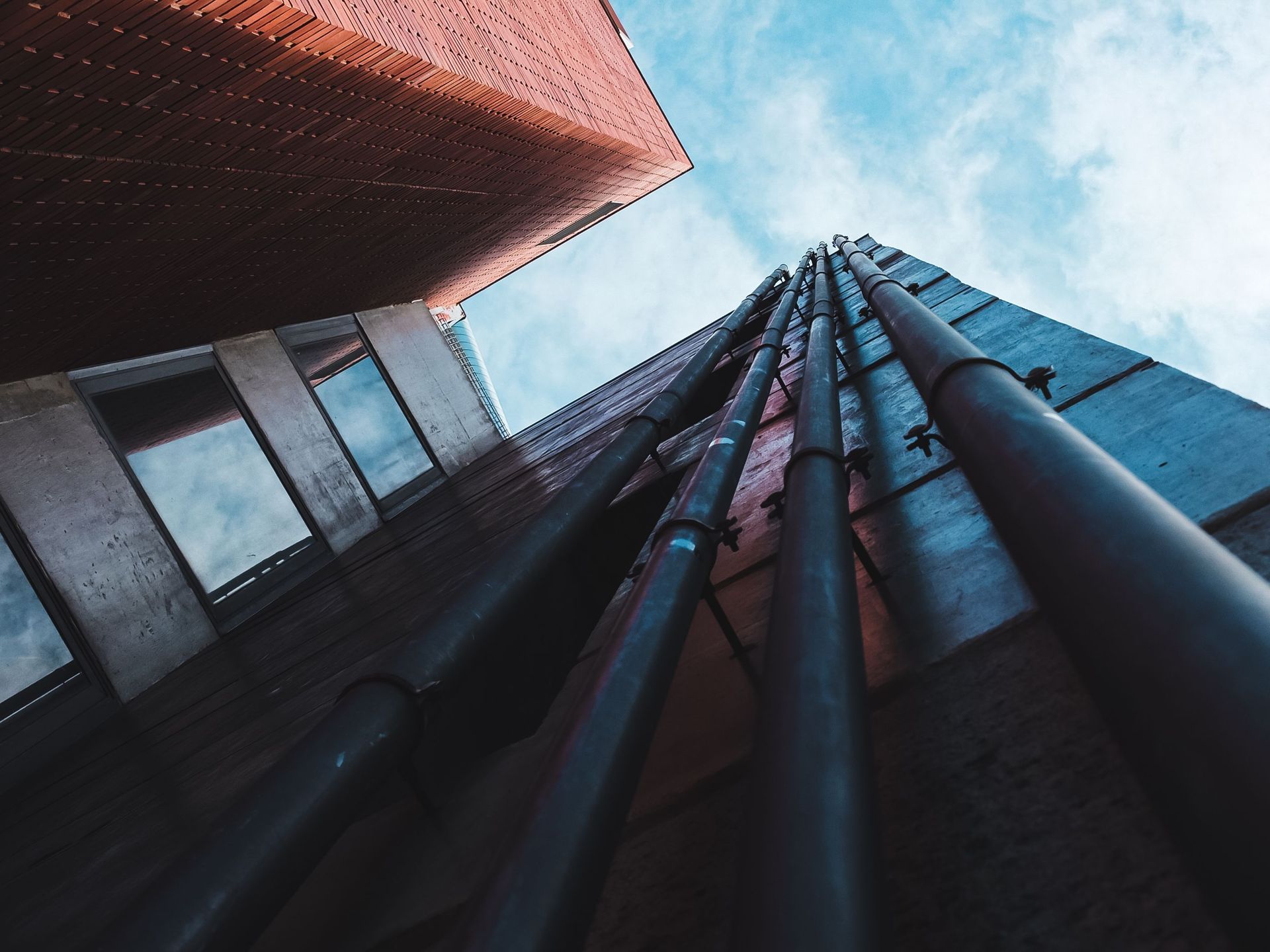 Four sewer pipes running up the side of a commercial building.
