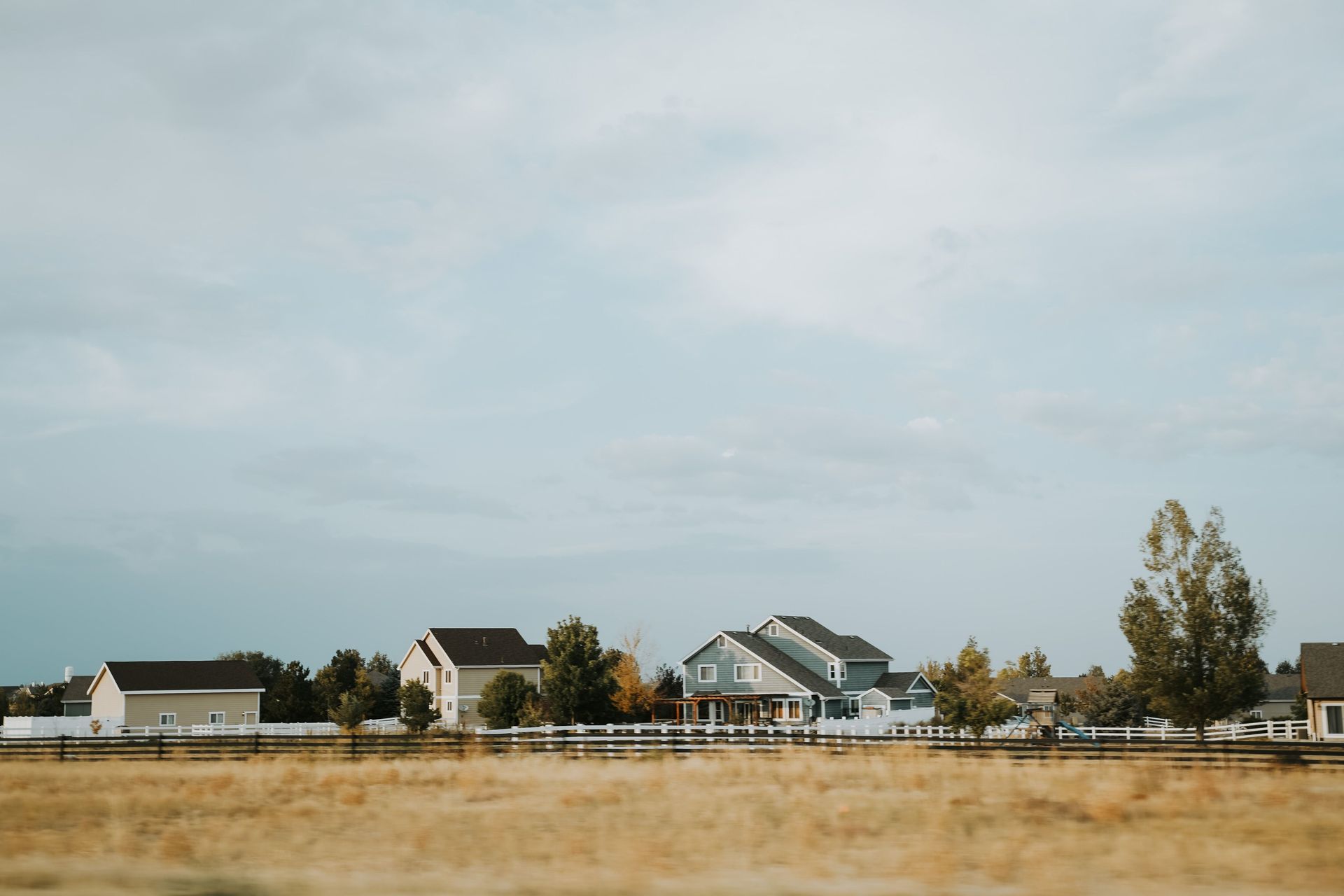 Rural single family homes surrounded by yellow grass and fenced-in yards