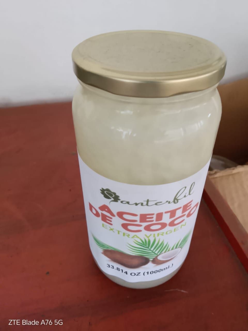 Frasco de crema de coco blanca con tapa dorada sobre una superficie roja