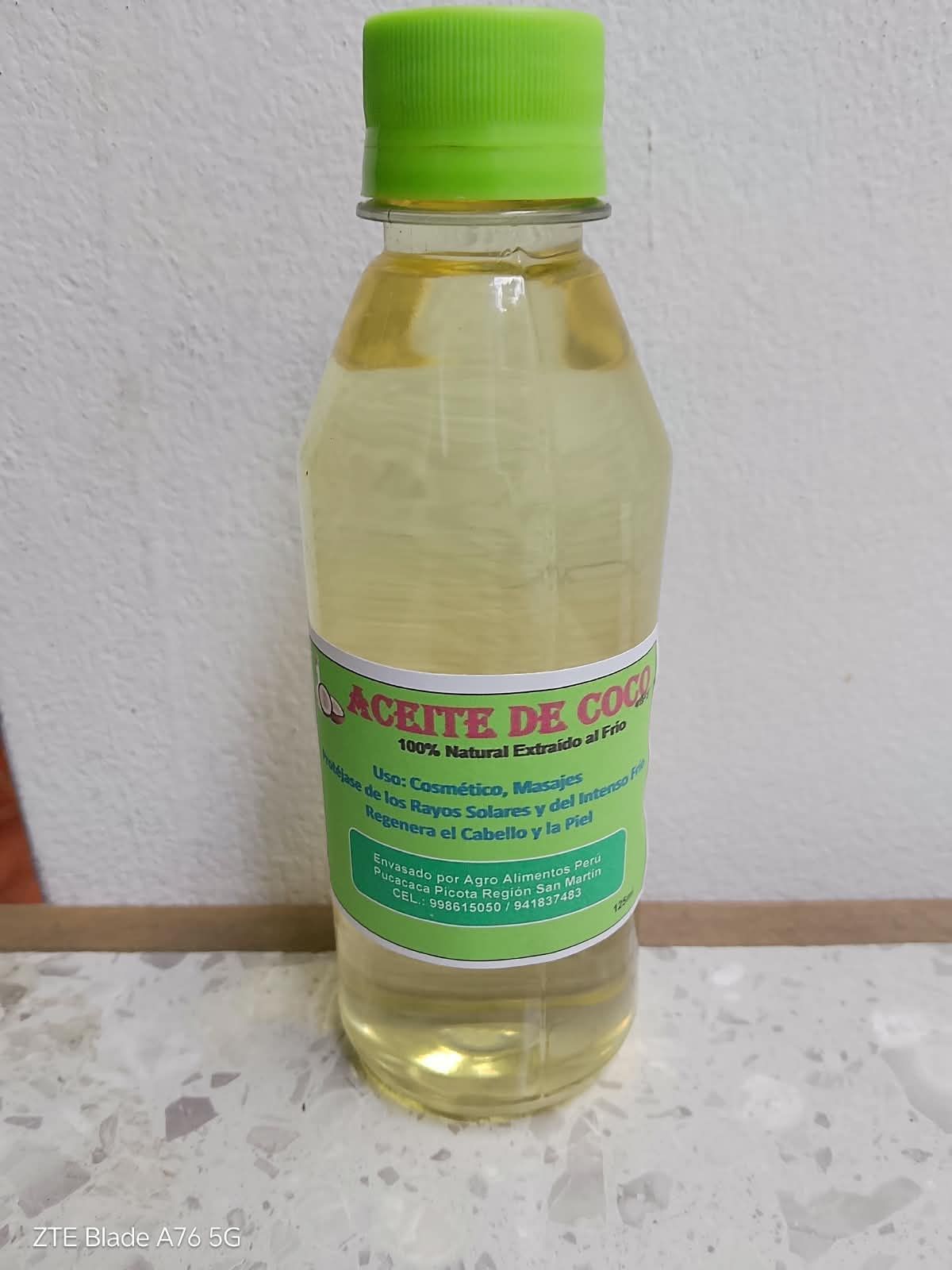 Botella de líquido amarillo transparente con tapón verde y etiqueta verde sobre una superficie blanca