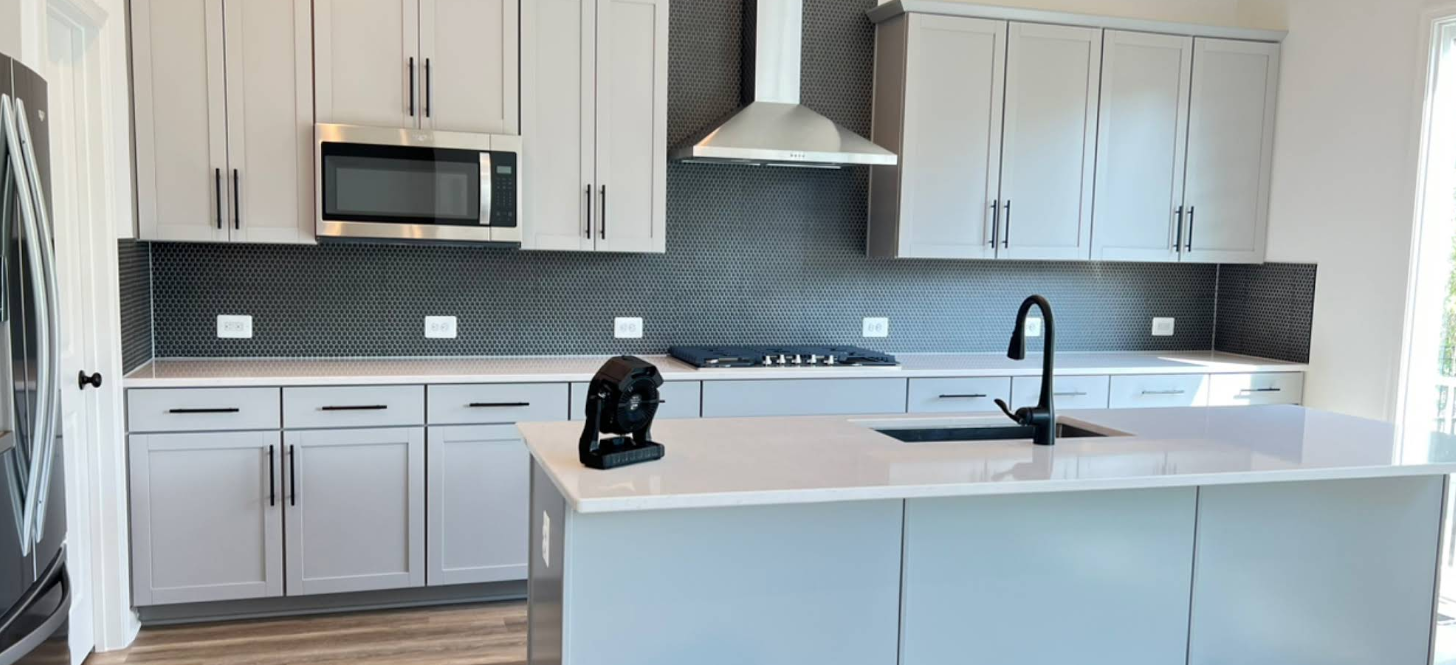 Modern kitchen with grey cabinets, white countertops, and a black backsplash.