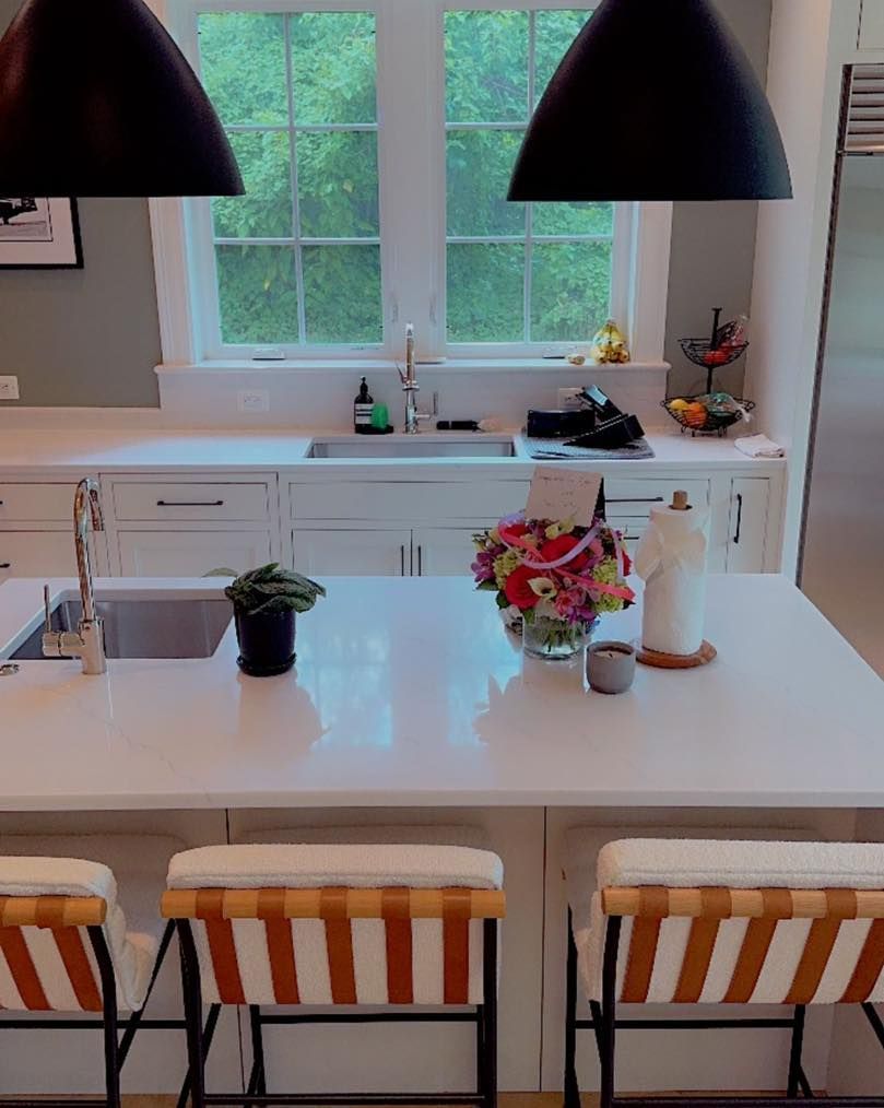 Bright kitchen with white island, striped stools, pendant lights, and flowers by a window