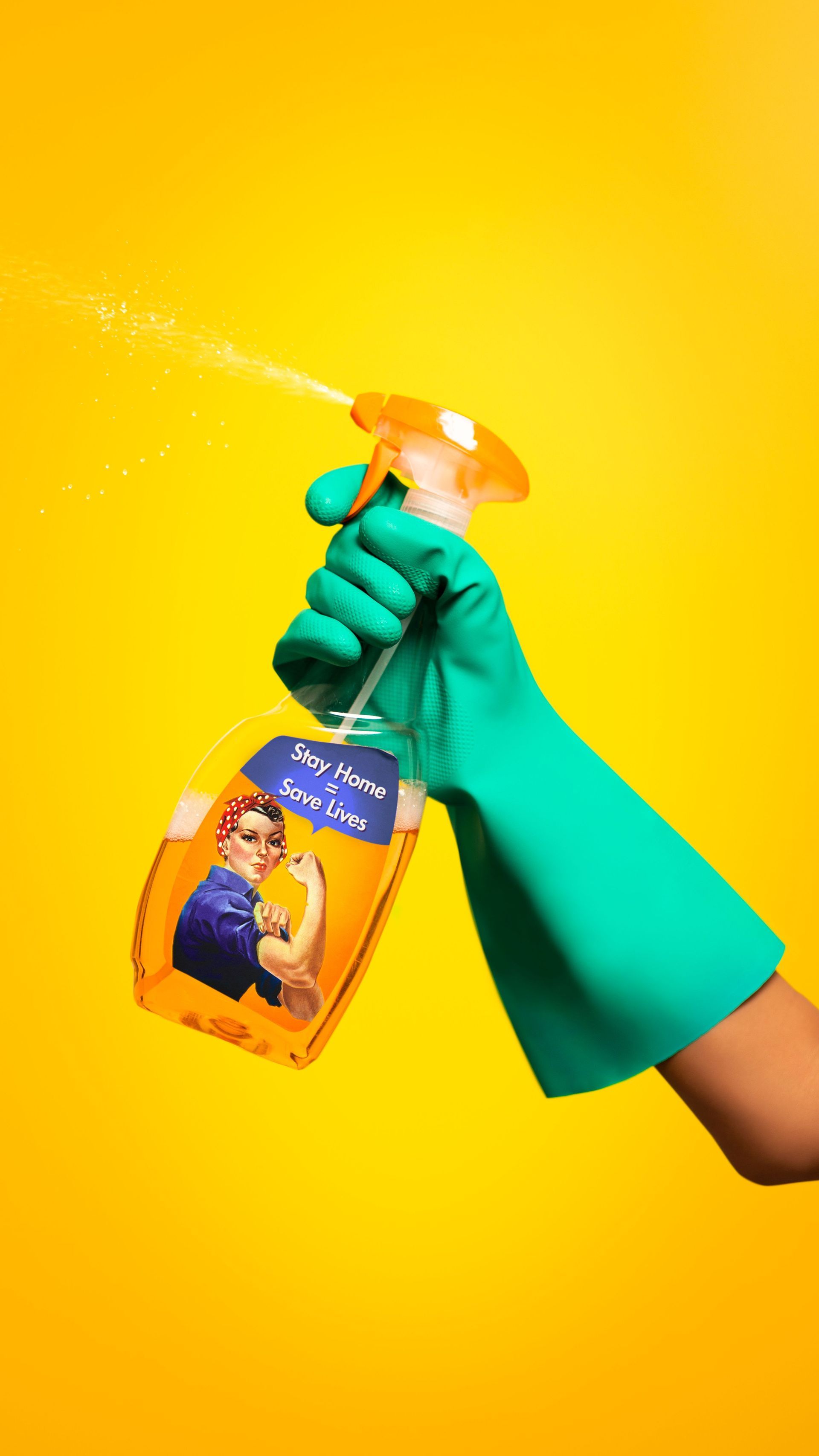 Green-gloved hand sprays cleaner from an orange bottle against a bright yellow background