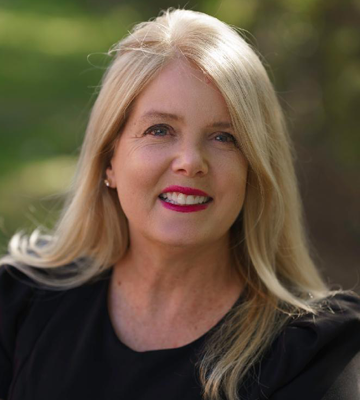 Smiling blonde woman in a black top outdoors with a blurred green background