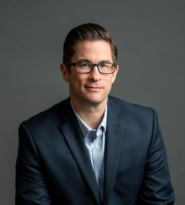 Studio portrait of a man in a navy suit and glasses against a gray background