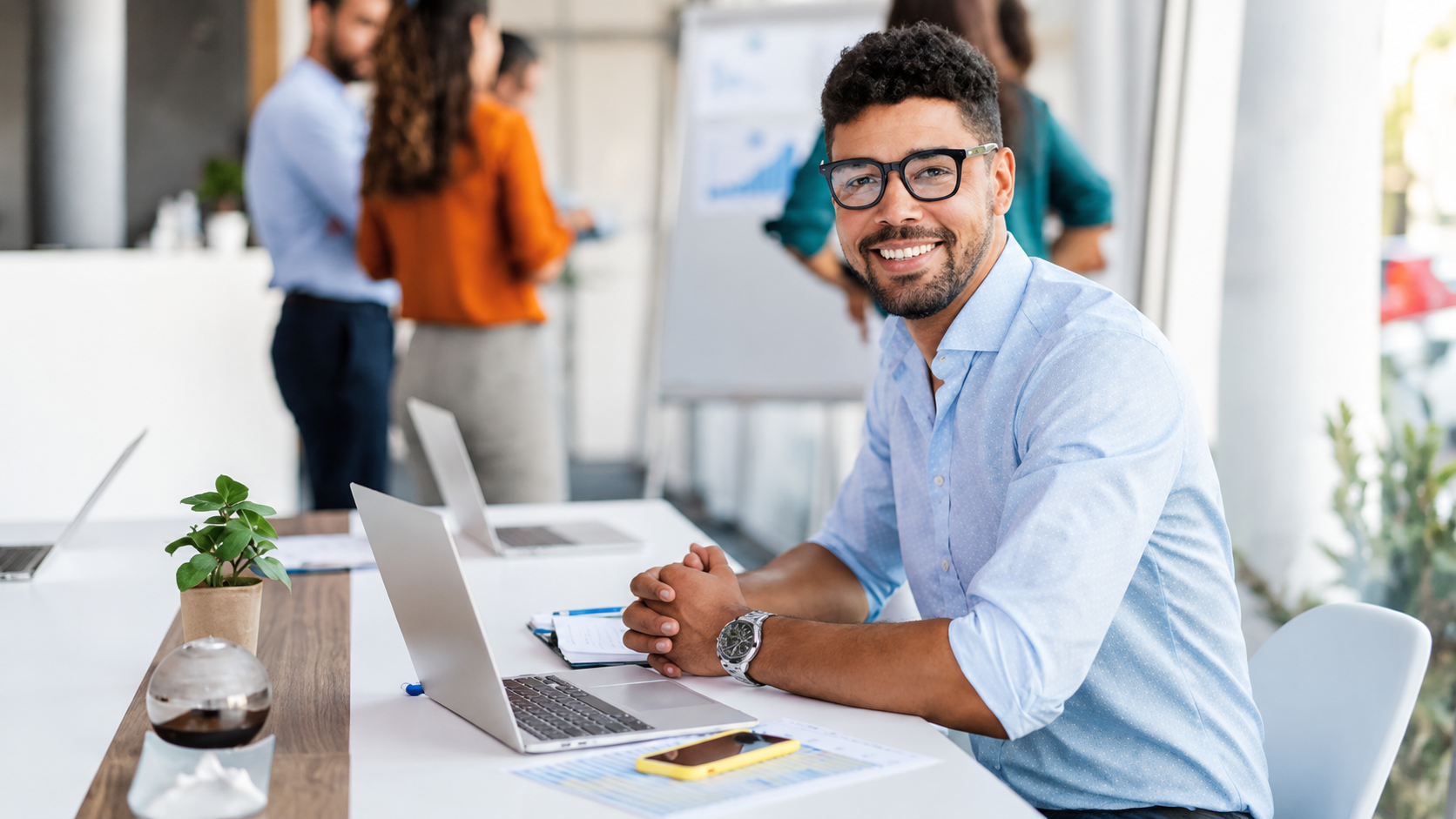 Smiling man with glasses working on a laptop at a desk in a bright office