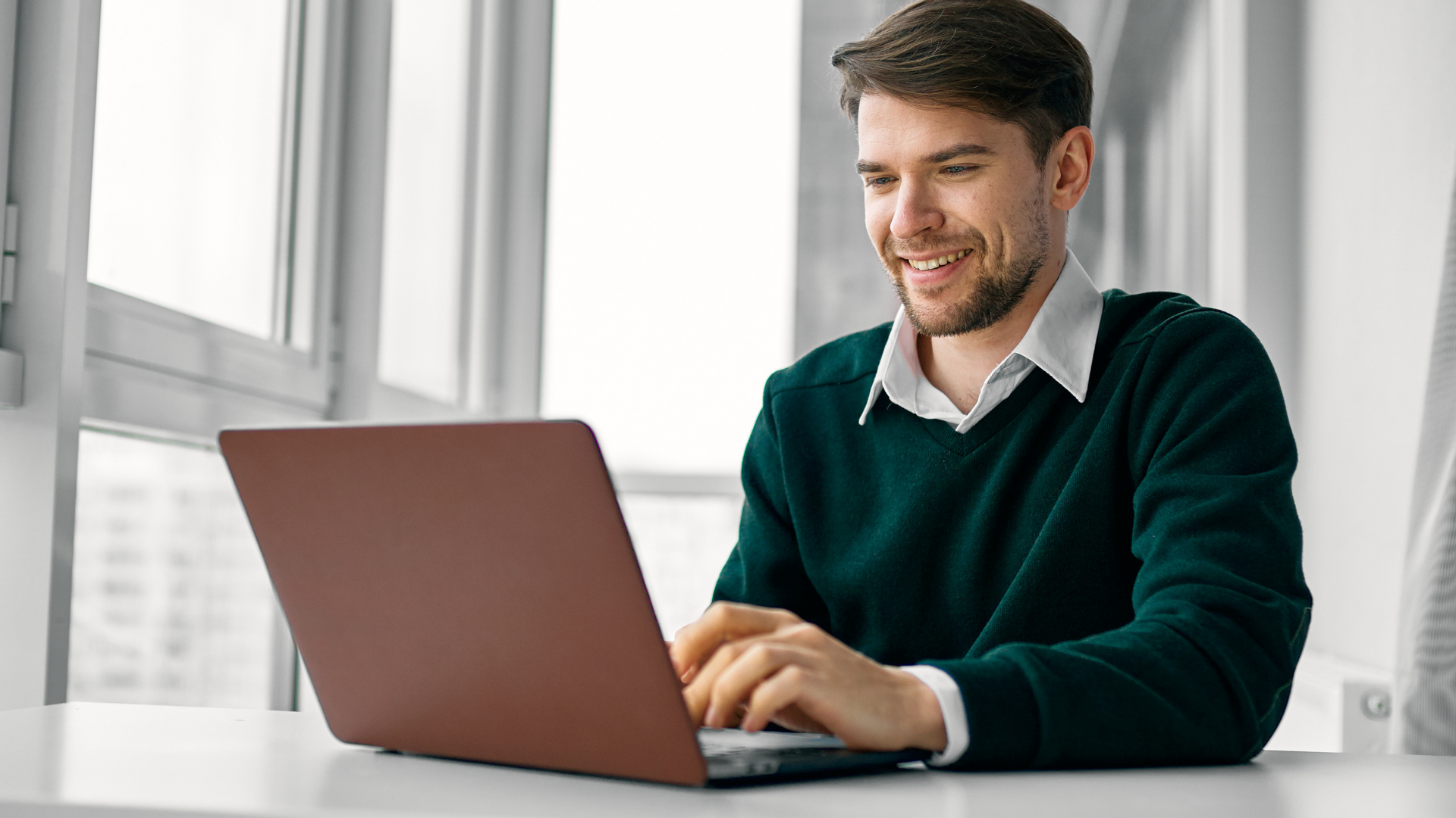 Person smiling at a desk with dual monitors and a calculator in a bright office