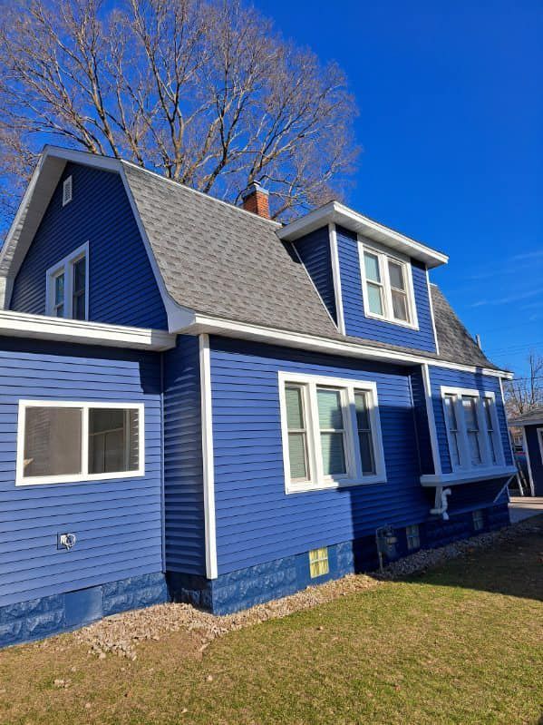 Blue house with white trim and steep roof under a clear blue sky, viewed from the side.