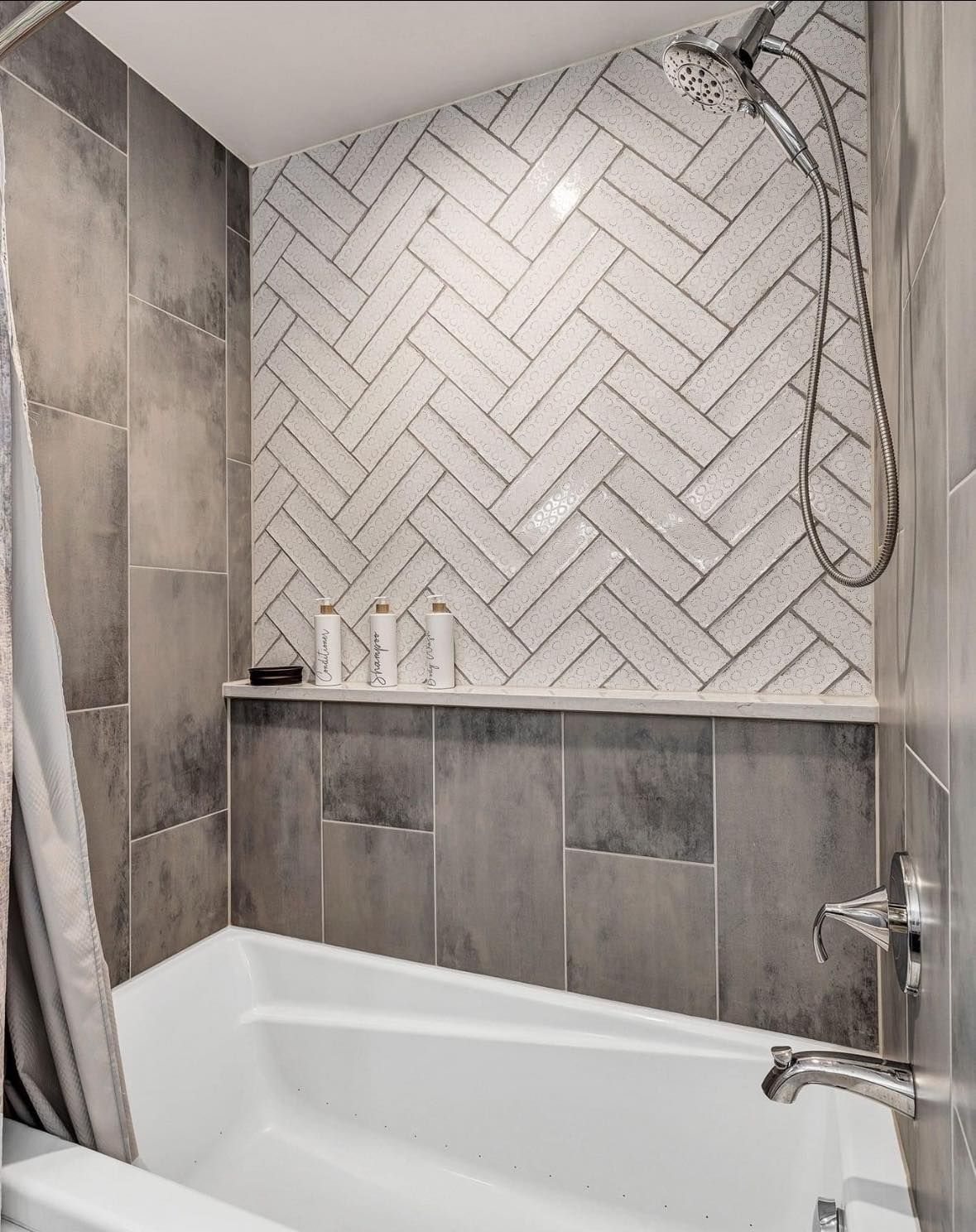 Modern bathroom with a white bathtub, gray tile walls, herringbone backsplash, and handheld showerhead