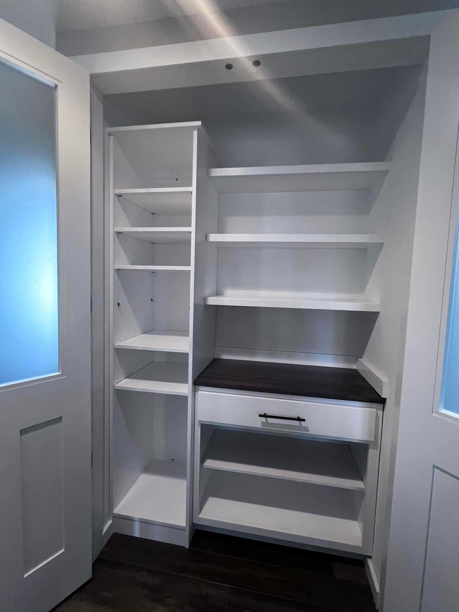 Built-in closet with white shelves, hanging rod, and drawers beside a doorway
