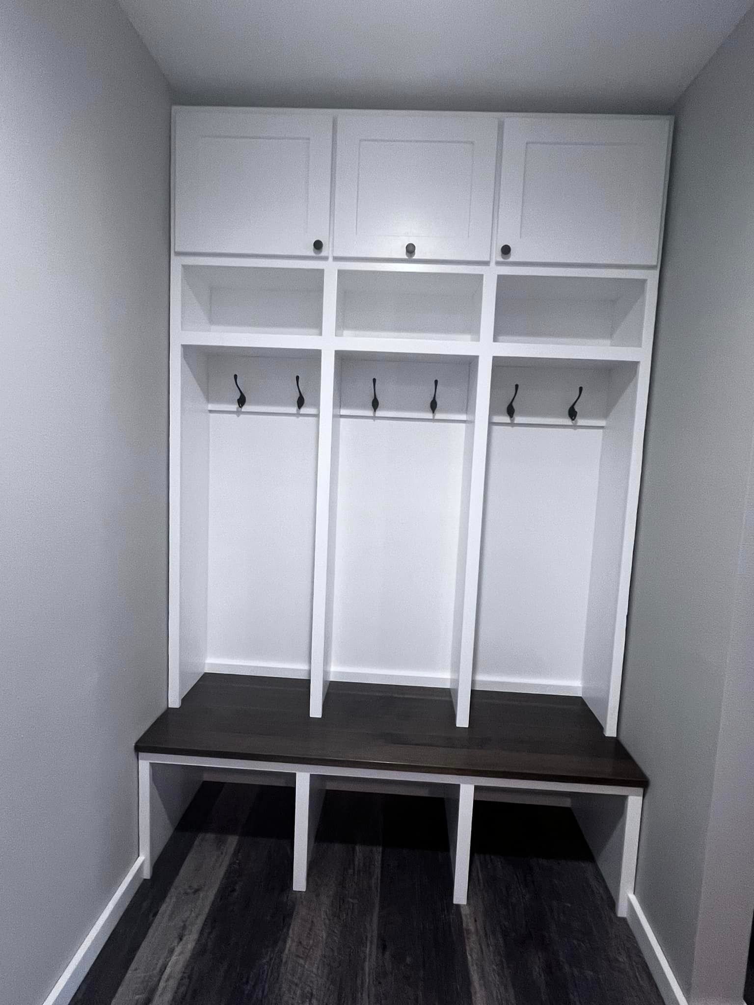 Built-in white closet with open shelves, hanging rods, and a dark bench in a small alcove.