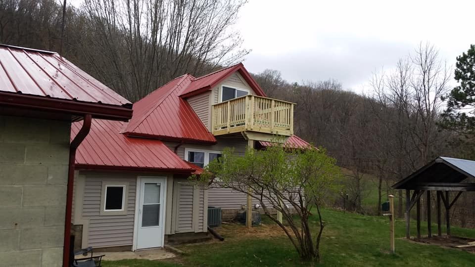 House with red roof and yellow balcony in a grassy yard with trees and a small gazebo