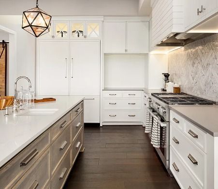 Bright modern kitchen with white cabinets, gray island, dark wood floor, and stainless steel stove.