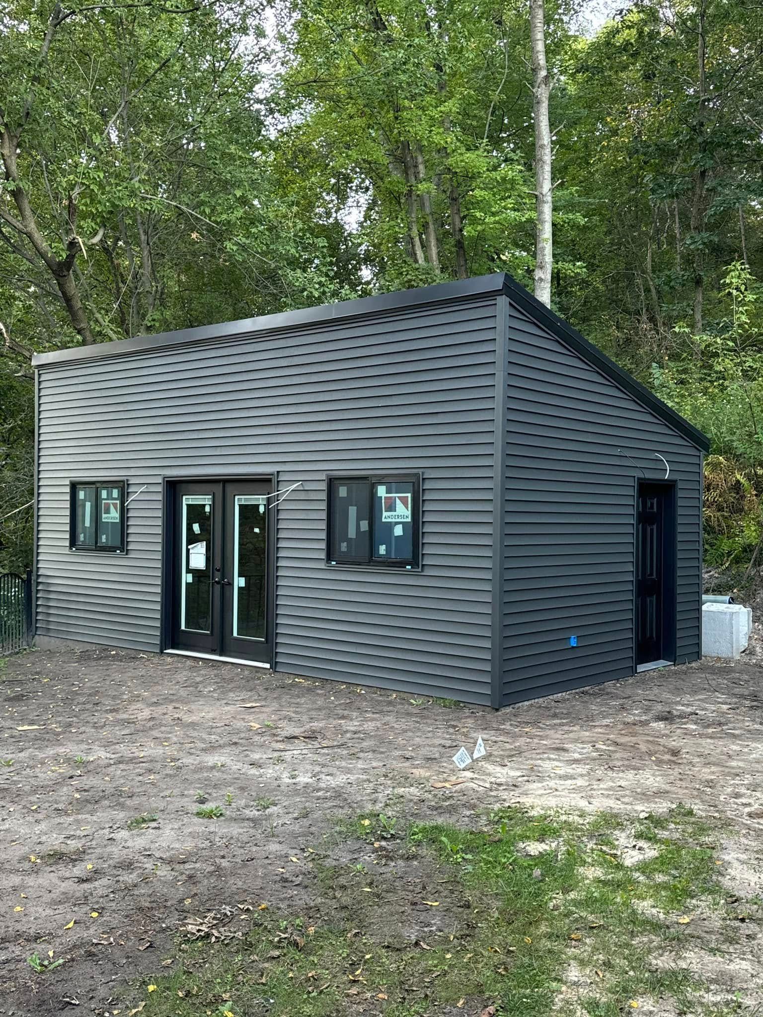 Dark gray cabin with black windows and doors in a wooded clearing