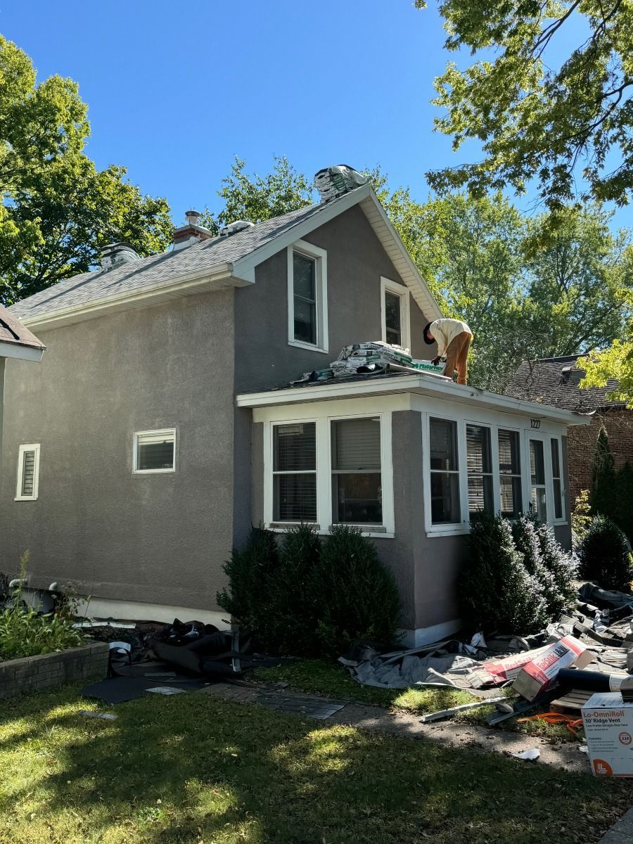 Two-story gray house with roof damage and scattered construction materials in the yard
