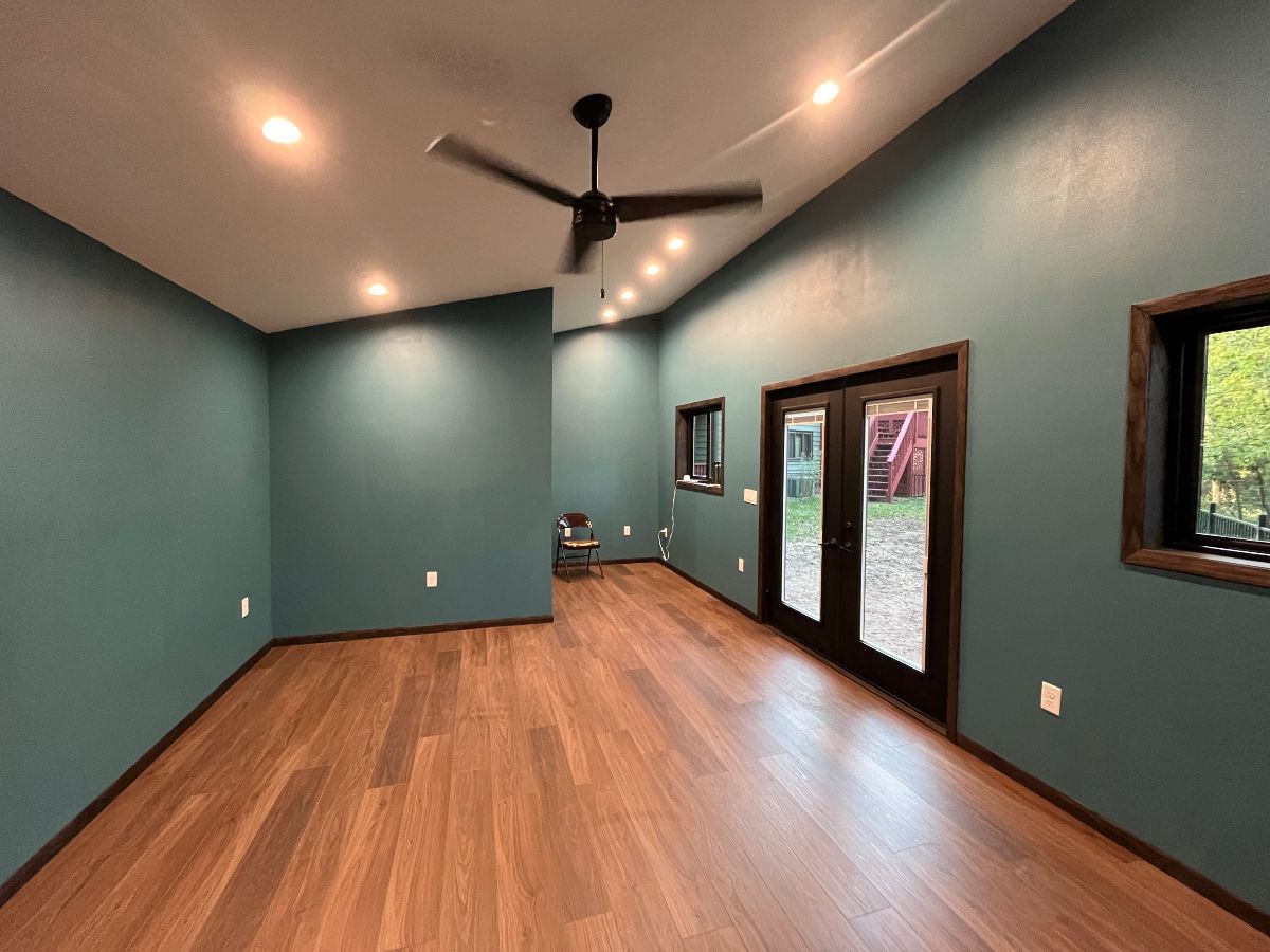 Empty living room with teal walls, wood floors, ceiling fan, and French doors to a patio.