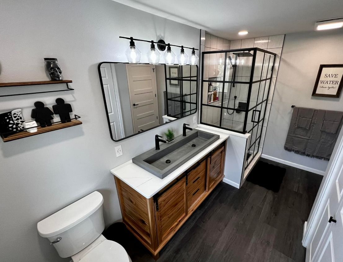 Modern bathroom with double vanity, black-framed shower, white toilet, and gray accents