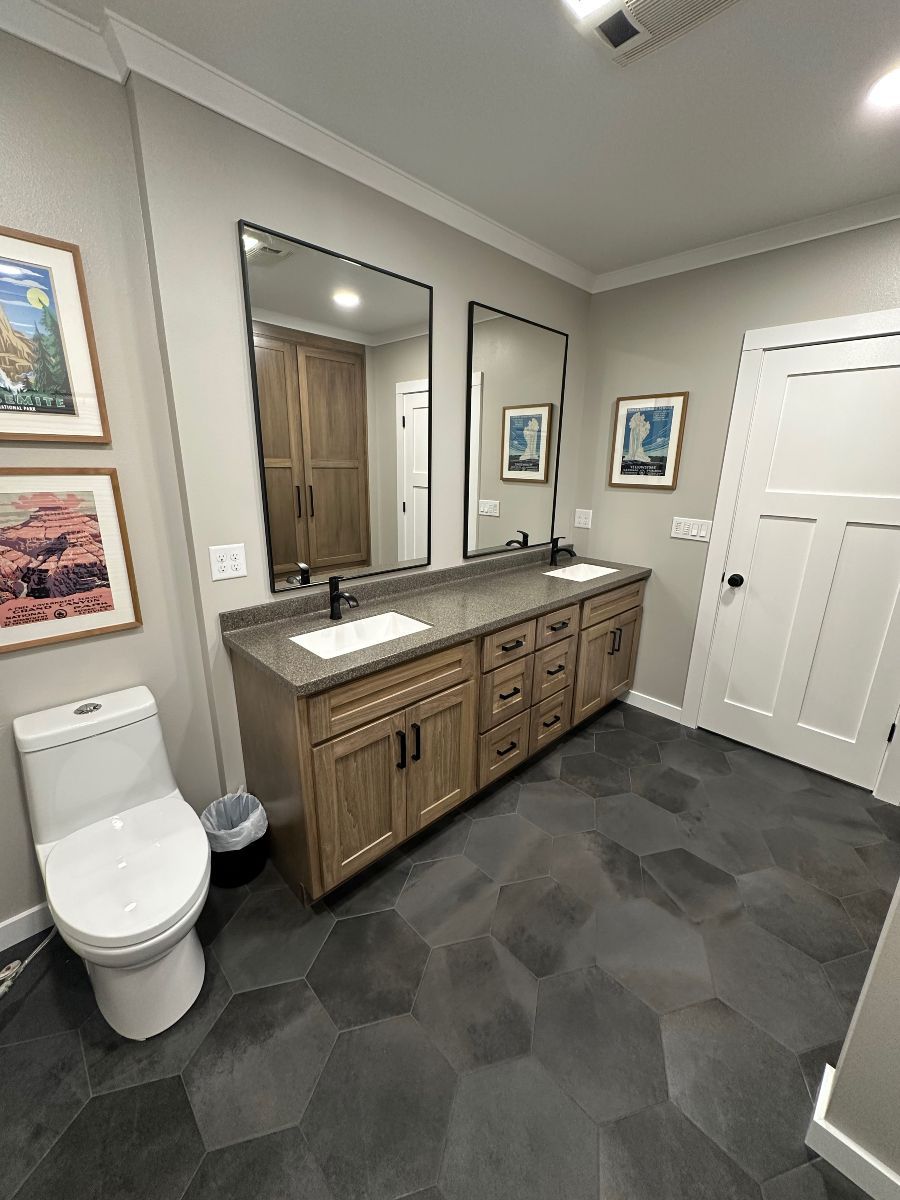 Modern bathroom with double vanity, large mirrors, white toilet, and dark hexagonal tile floor.
