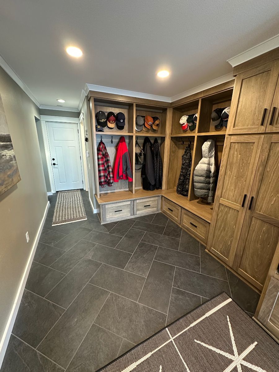 Entryway mudroom with built-in wood cubbies, coats, shoes, and dark tile floor