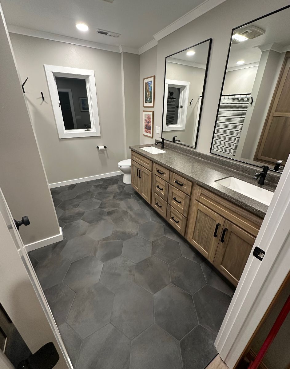 Modern bathroom with double vanity, large mirror, gray tile floor, and window.
